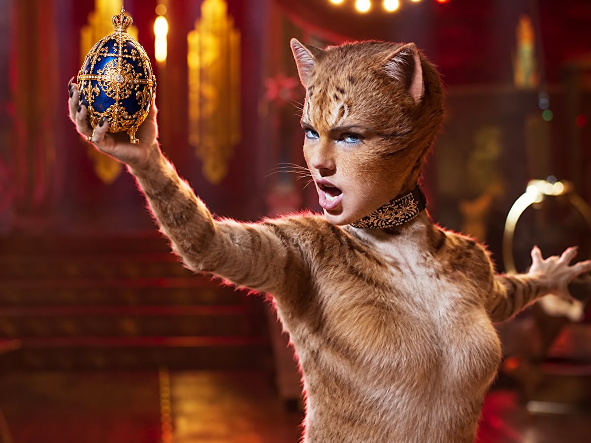 Fictional theatrical illustration of a feline performer holding an ornate blue-and-gold jeweled egg beneath warm stage lights.
